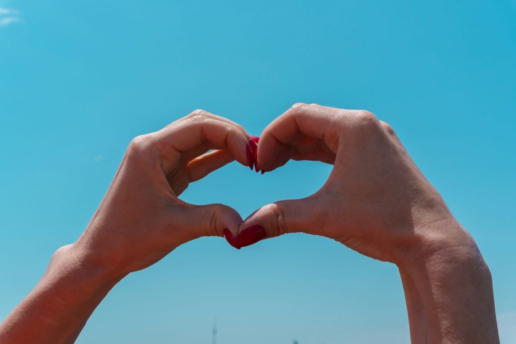 Hands forming a heart shape against blue sky.